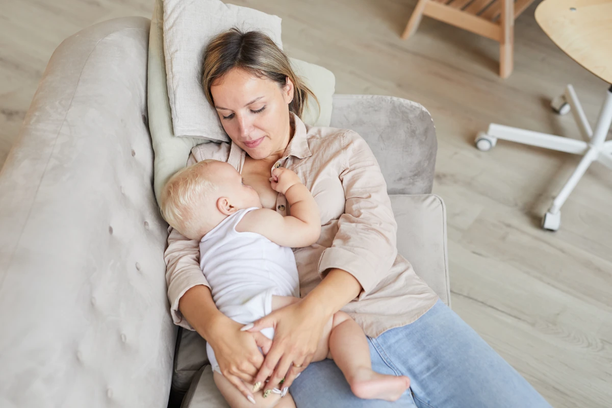 Une maman qui allaite son bébé allongé dans un canapé