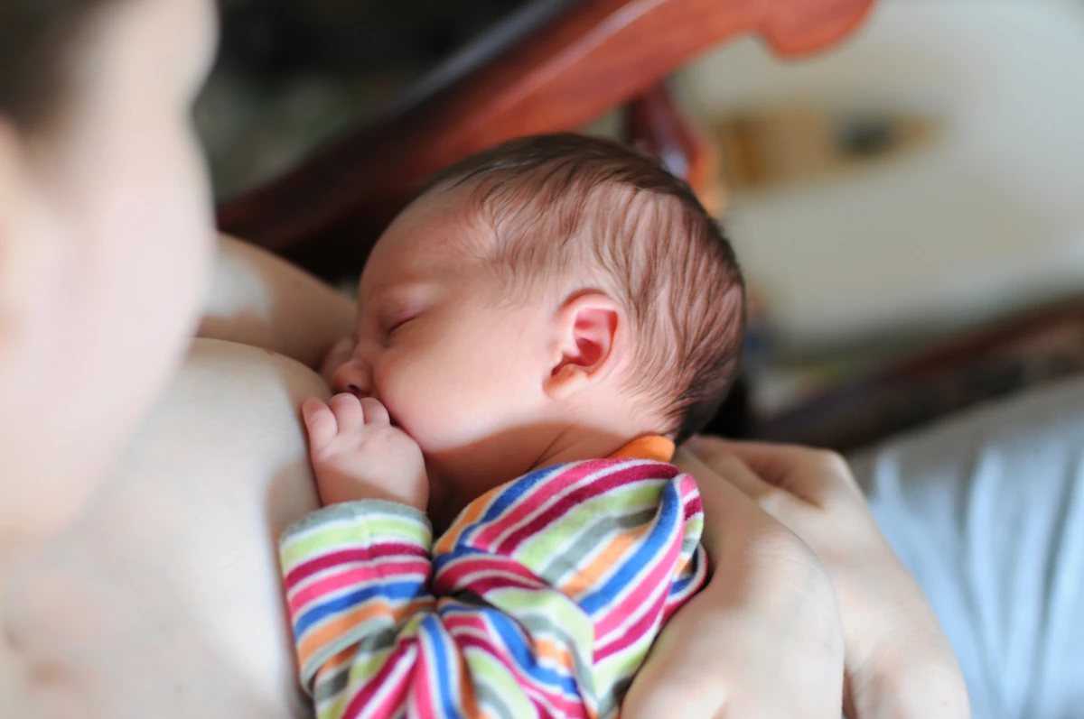 Une femme qui tient la tête de son bébé pendant un allaitement 