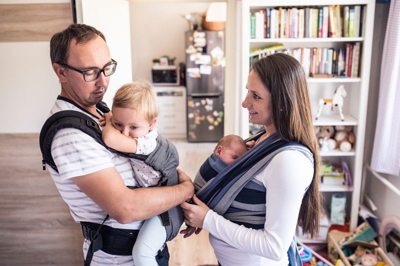 Parents avec bébé en écharpe de portage et poussette